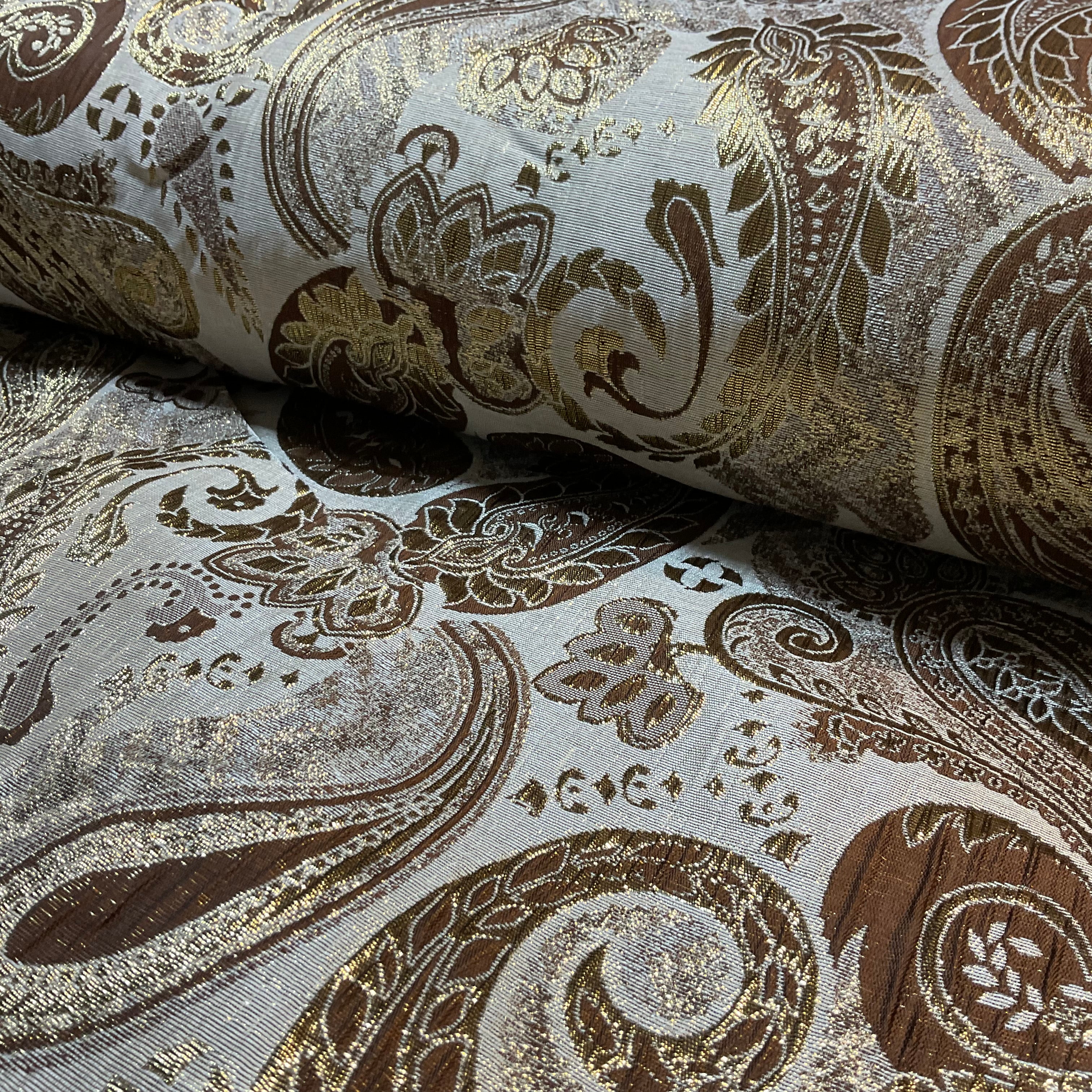 Roll of decorative fabric with intricate paisley pattern in brown and gold on a gray background