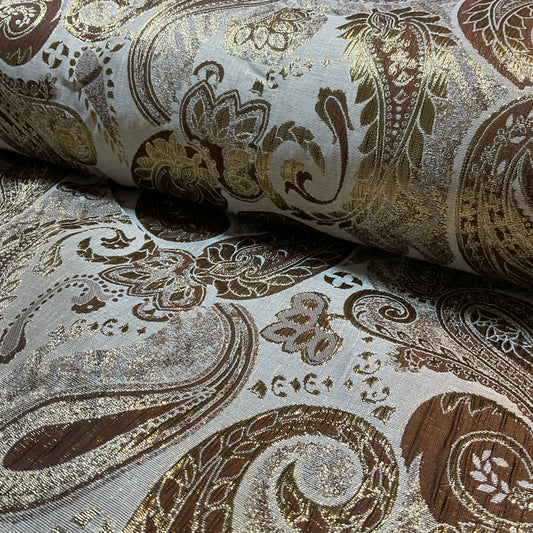 Roll of decorative fabric with intricate paisley pattern in brown and gold on a gray background