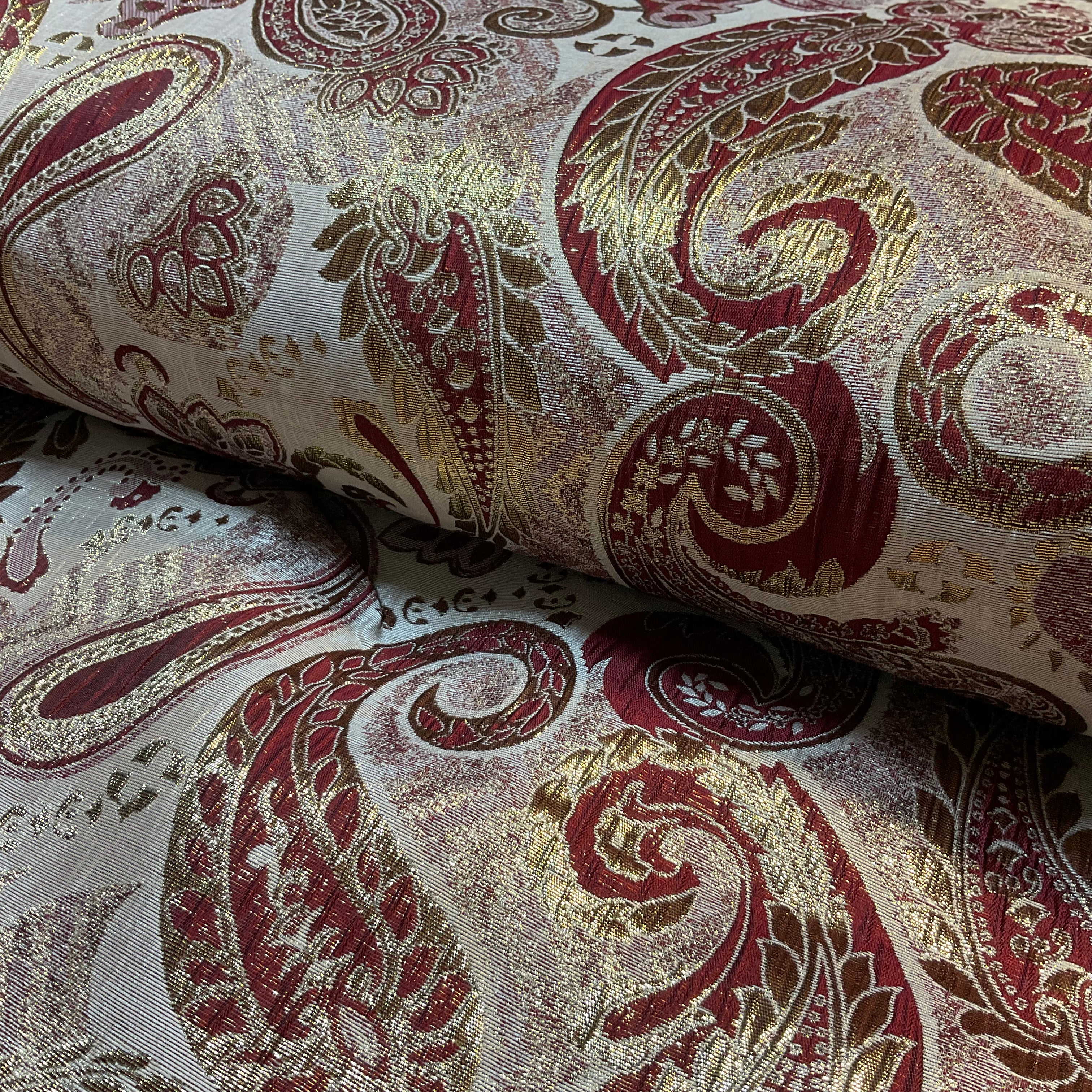 Close-up of patterned fabric with red and gold designs on a beige background