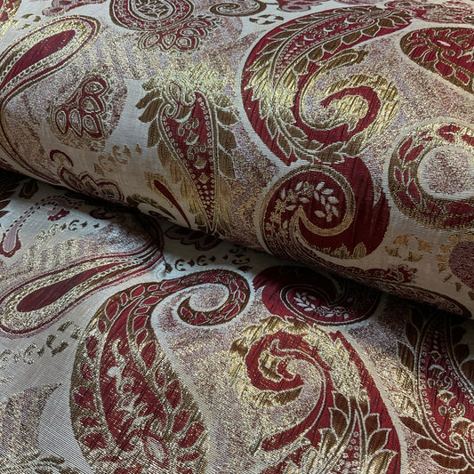 Close-up of patterned fabric with red and gold designs on a beige background
