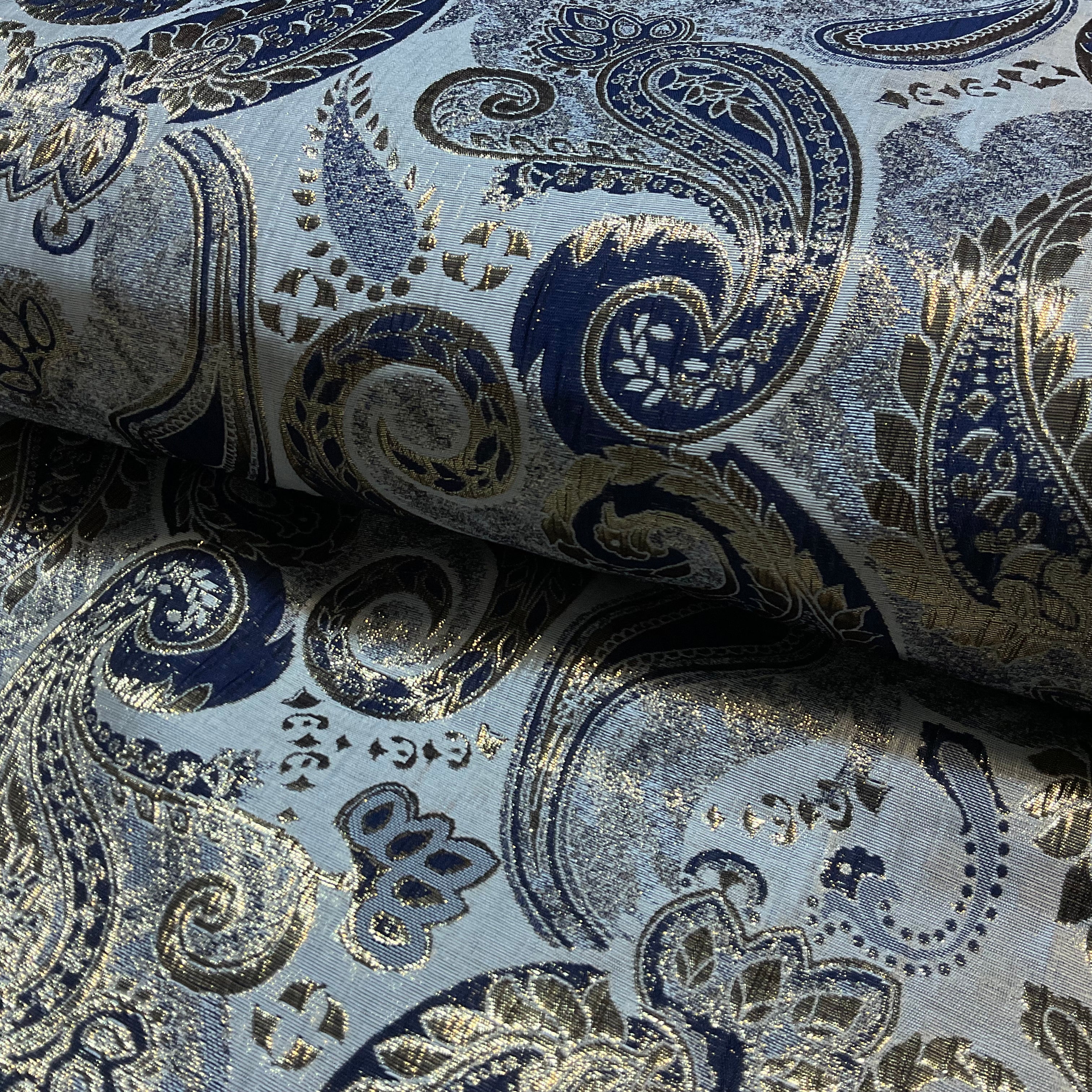 Roll of fabric with intricate paisley pattern in blue and gold on a light gray background