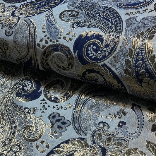 Roll of fabric with intricate paisley pattern in blue and gold on a light gray background